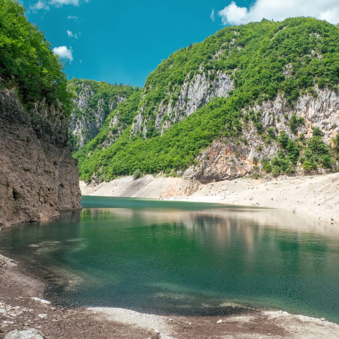 a body of water with a rocky cliff and trees on the side