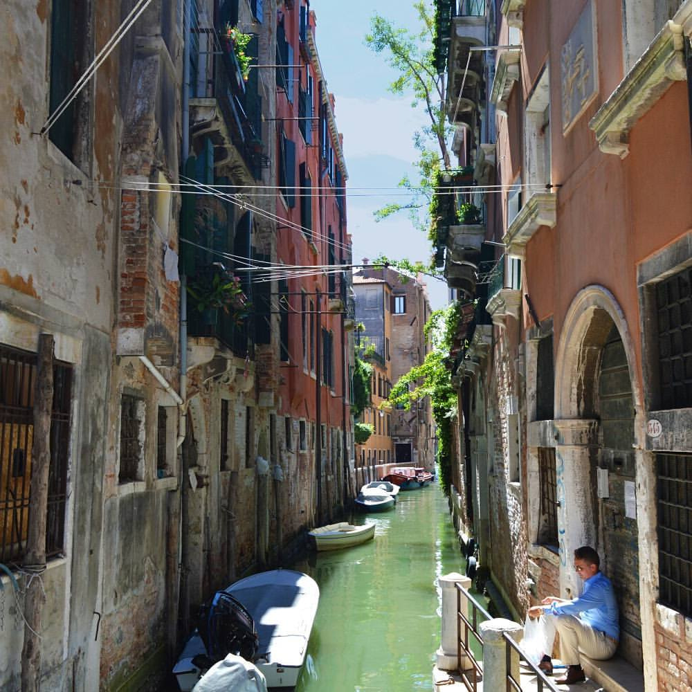a person sitting on a bench next to a canal with boats